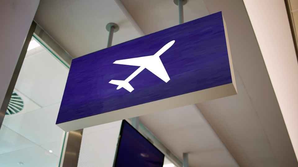 Panneau d'aéroport avec une icône d'avion blanc indiquant la direction des départs de vols.