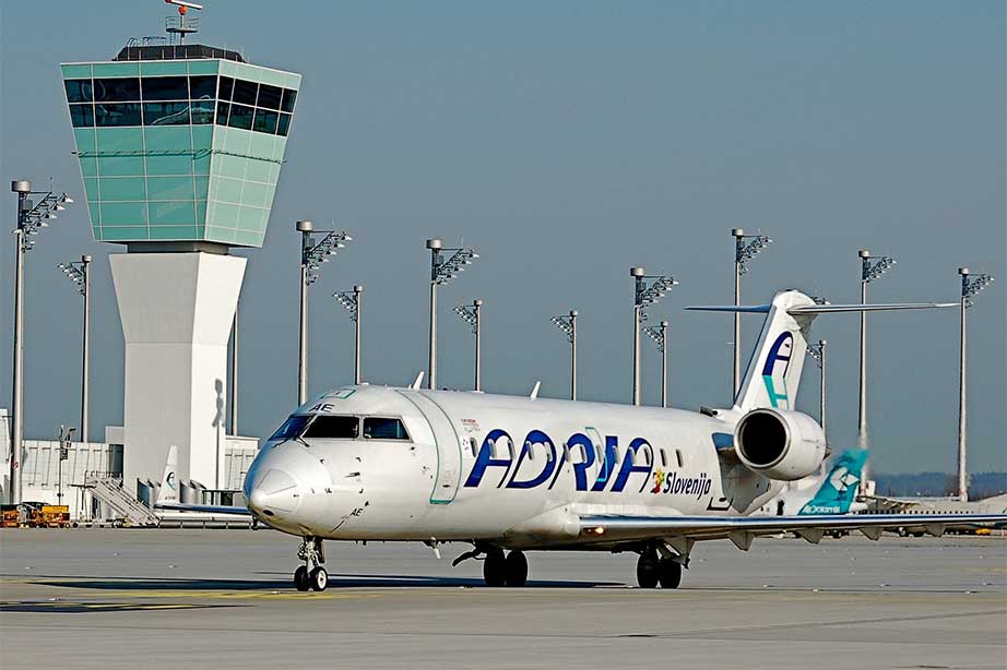 adria airways plane on runway next to traffic tower