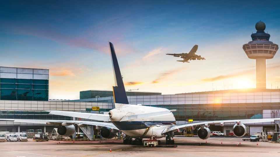 Airplanes at the airport with a departing flight taking off near the control tower at sunrise.