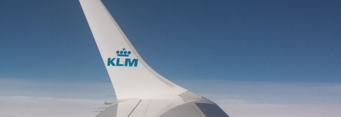 KLM aircraft wing above a blanket of clouds under a clear blue sky.