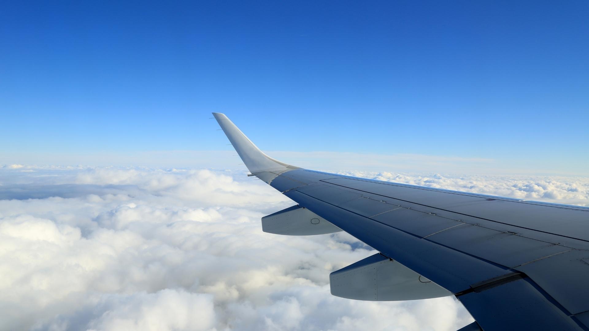 Aircraft wing above the clouds with a clear blue sky.