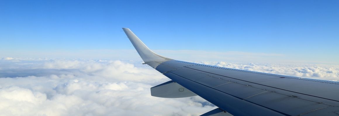 Aircraft wing above the clouds with a clear blue sky.