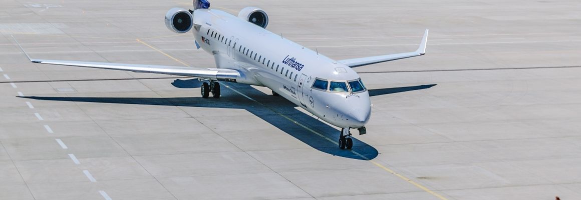 A Lufthansa regional jet taxiing on the airport apron, captured from above on a sunny day.