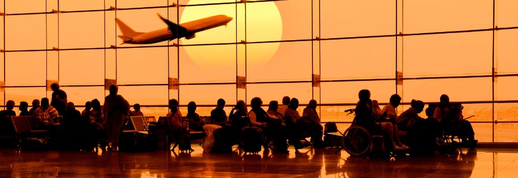 Passagers attendant dans un terminal d'aéroport au coucher du soleil, regardant un avion en partance à travers la grande fenêtre.